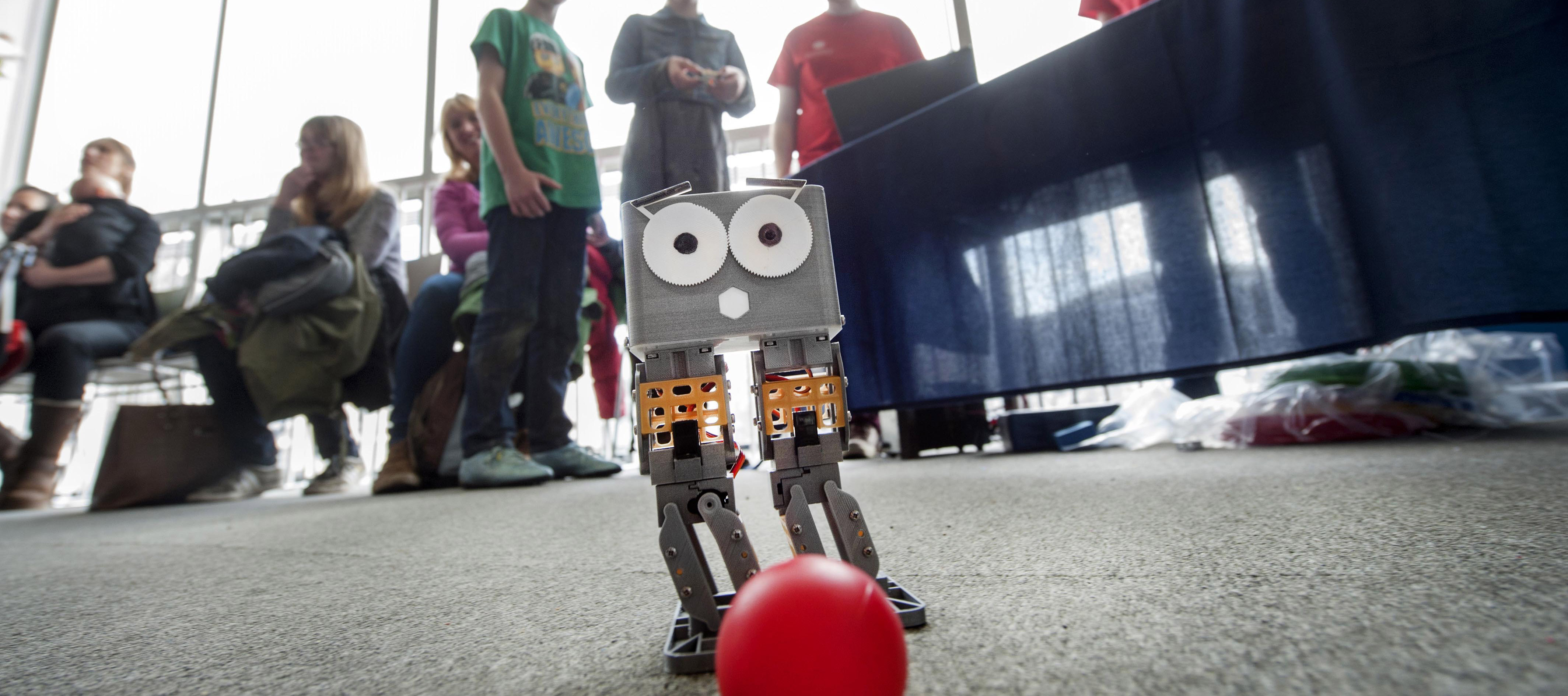 A robot controlled by children plays with a football
